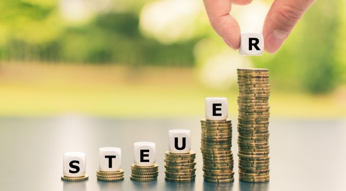 Würfel formen das Wort Steuer auf aufsteigenden Münzstapeln